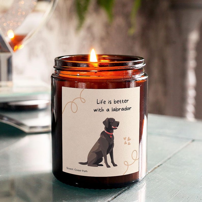 Pode incluir: Uma vela de vidro &acirc;mbar acesa com um r&oacute;tulo com uma ilustra&ccedil;&atilde;o de um labrador preto e o texto "Life is better with a labrador". A vela tem uma chama brilhante. A fragr&acirc;ncia &eacute; "Coast Path".