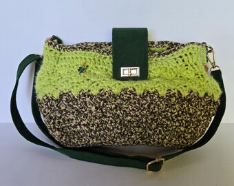 May include: A handmade crochet shoulder bag in green and brown. The bag has a flap closure with a gold-coloured clasp and a dark green adjustable strap. A small gold-coloured charm with a green accent is attached to the bag.