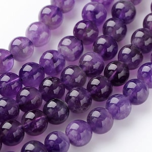 Könnte beinhalten: Eine Reihe runder, violetter Amethystperlen. Die Perlen sind glatt und poliert, mit einer leichten Farbabweichung.