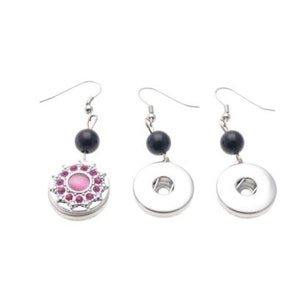 Könnte beinhalten: Drei silberfarbene Hängeohrringe. Ein Ohrring hat eine rosa Mitte, die von rosa Edelsteinen und einem silbernen Rand umgeben ist. Die anderen beiden Ohrringe haben ein silbernes Scheibendesign. Jeder Ohrring hat eine schwarze Perle und einen silbernen Haken.