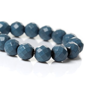 Può includere: Una collana di perline di vetro sfaccettate blu scuro. Le perline sono rotonde e hanno una superficie testurizzata.
