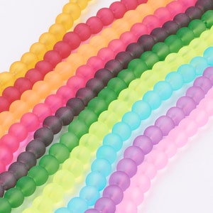 Può includere: Un assortimento di perline di vetro smerigliato arcobaleno. Le perline sono disposte in file, ogni fila di un colore diverso. I colori sono rosa, viola, blu, verde, giallo, arancione e rosso.
