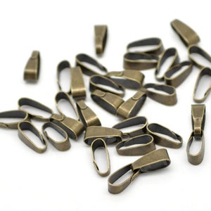 May include: A collection of antique bronze-colored pendant bails, scattered on a white surface. The bails have a loop shape with a small, rectangular top for attaching to a chain or cord. Ideal for jewelry making.