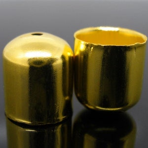 Könnte beinhalten: Zwei goldfarbene Flaschenverschlüsse aus Metall. Die Verschlüsse sind rund und haben eine glatte, glänzende Oberfläche.