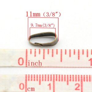 May include: A small, antique brass-colored metal finding, measuring 11mm (3/8") in length and 9.7mm (3/8") across. The image includes a measuring tape with inch and centimeter markings, and text indicating the dimensions.