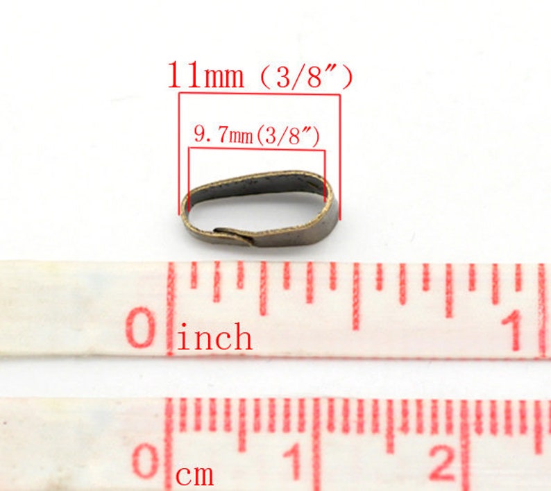 May include: A small, antique brass-colored metal finding, measuring 11mm (3/8") in length and 9.7mm (3/8") across. The image includes a measuring tape with inch and centimeter markings, and text indicating the dimensions.