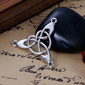 Könnte beinhalten: Silberner keltischer Knoten-Anhänger mit drei Schlaufen. Der Anhänger hat eine dreieckige Form und ist mit komplizierten Knotenarbeiten verziert.