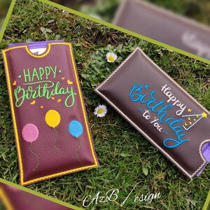 May include: Two brown leather gift card holders with embroidered birthday greetings. One holder has the text "Happy Birthday" with colourful balloons. The other holder has the text "Happy Birthday to You" with a star and a party hat.