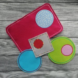 May include: Four felt circles with different designs. One is pink with a white snowflake design, one is green with a pink and white gingham design, one is grey with a red polka dot design, and one is blue.