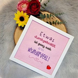 Könnte beinhalten: Ein weiß gerahmter rosa Leinwand mit dem Text "Etwas durchgeknallt ist ganz nah an wundervoll!" in lila und rosa Schrift. Ein kleines rotes Herz befindet sich in der rechten unteren Ecke.