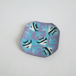 May include: A small, decorative ceramic dish with a purple and blue glaze. The dish has a geometric shape and features a pattern of black and white stripes.