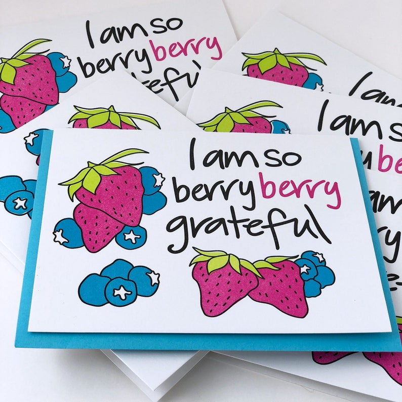 A flat lay image of several greeting cards with the image of strawberries and blueberries and the words I am so berry berry grateful.