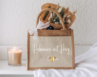 Puede incluir: Una bolsa de yute marrón con una etiqueta blanca que dice "Hebamme mit Herz" y "Claudia" con un corazón dorado. La bolsa está llena de flores secas y una cinta de encaje blanca.