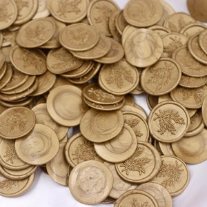 Op de afbeelding: Een stapel gouden waszegels met een bladerenontwerp. De zegels zijn rond en hebben een gladde, glanzende afwerking.