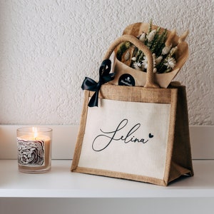 May include: A personalized jute tote bag with a black ribbon and the name "Selina" printed on the front. The bag is filled with a bouquet of dried flowers.