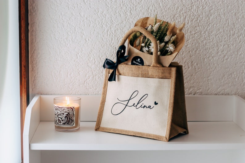 May include: A personalized jute tote bag with a black ribbon and the name "Selina" printed on the front. The bag is filled with a bouquet of dried flowers.