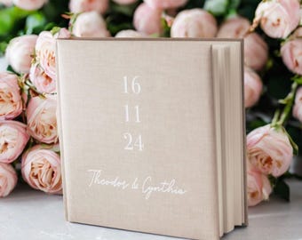 May include: A beige linen-covered photo album with the numbers 16, 11, and 24 printed in white on the front. The album also has the text "Theodor & Cynthia" printed in white on the front.