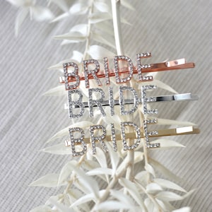 Könnte beinhalten: Drei Haarklammern in Gold, Silber und Roségold mit dem Wort "BRIDE" in Strasssteinen.