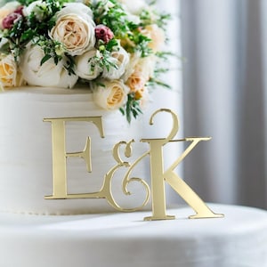 Könnte beinhalten: Goldfarbener, spiegelnder Acryl-Kuchentopper mit den Buchstaben E & K, perfekt für eine Hochzeit oder eine Jubiläumsfeier.