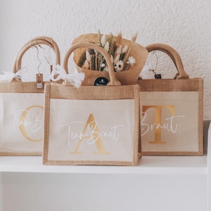 Puede incluir: Tres bolsas de yute marrón con letras blancas y detalles en dorado. Las bolsas están decoradas con las palabras "Team Braut" y "Braut".