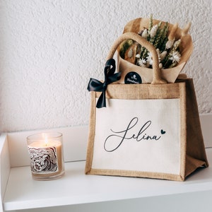 May include: A personalized jute tote bag with the name "Selina" printed in black script with a small heart. The bag is filled with a bouquet of dried flowers and a black ribbon.
