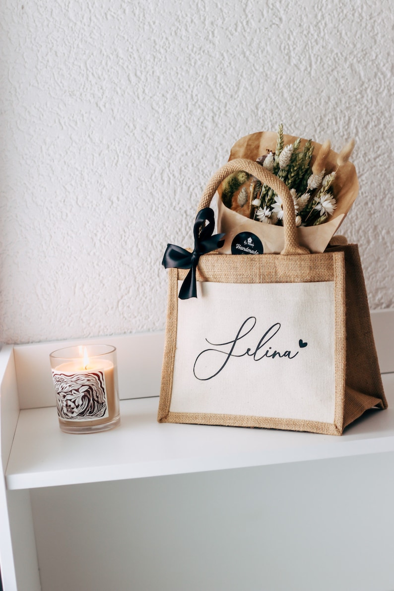 May include: A personalized jute tote bag with the name "Selina" printed in black script with a small heart. The bag is filled with a bouquet of dried flowers and a black ribbon.