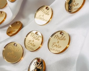 以下が含まれることがあります： 「Melike & Emre」と日付「10.05.2024」が刻まれた、ゴールドの丸いアクリル製の結婚式のお礼タグです。