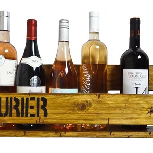 May include: A wooden wine rack with the word "VINOSAURIER" stenciled on the front. The rack holds six bottles of wine, including red, white, and ros&eacute;.