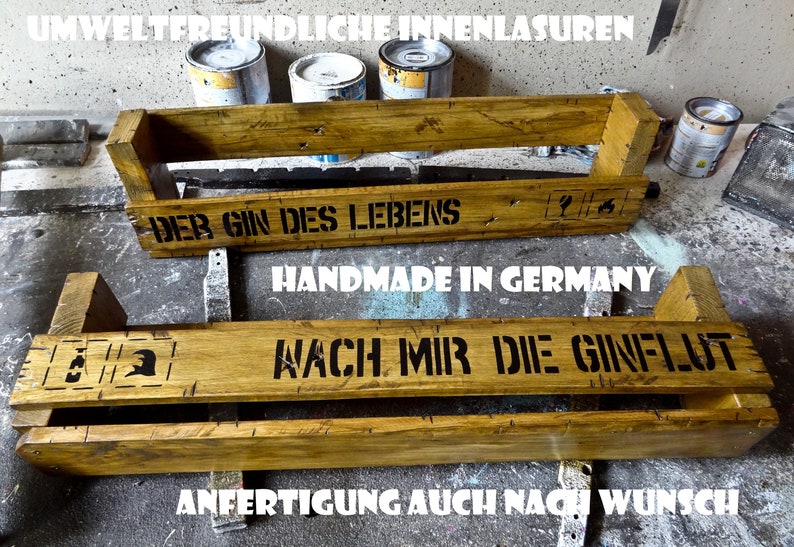 May include: Two wooden shelves with the text "Der Gin des Lebens" and "Handmade in Germany" on the top shelf and "Wach mir die Gin-Flut" on the bottom shelf. The shelves are stained a light brown color and have a rustic appearance.