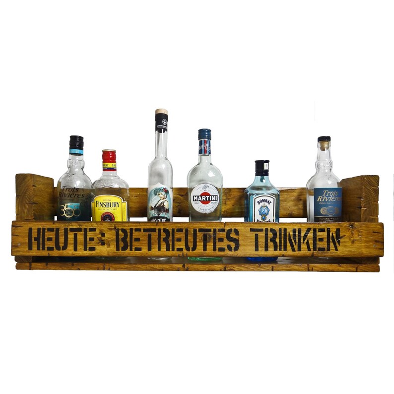 May include: A wooden wall-mounted shelf with a sign that reads "HEUTE BETREUTES TRINKEN" and six bottles of liquor, including a bottle of gin, a bottle of martini, and a bottle of whiskey.