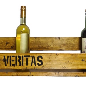 May include: Wooden wine rack with the text "In Vino Veritas" on the front. The rack has four slots for bottles and is made of reclaimed wood. There are four bottles of wine in the rack, two red and two white.