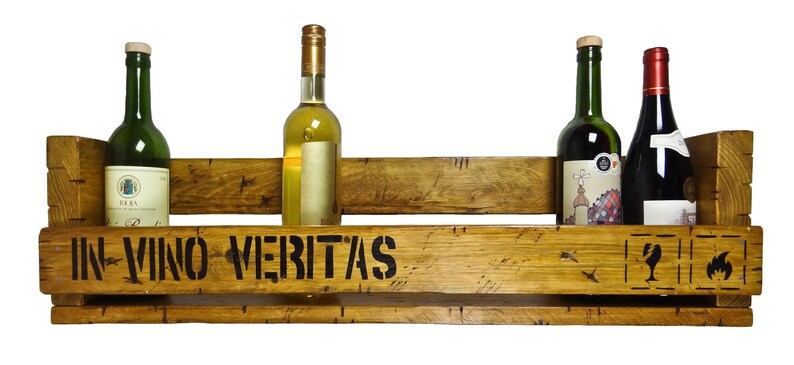 May include: Wooden wine rack with the text "In Vino Veritas" on the front. The rack has four slots for bottles and is made of reclaimed wood. There are four bottles of wine in the rack, two red and two white.