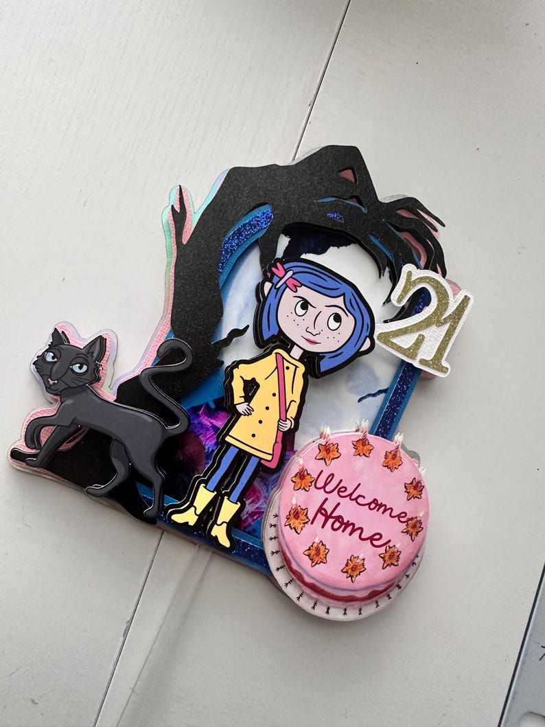 May include: A colorful cake topper featuring a girl with blue hair and a yellow raincoat, a black cat, a hand reaching down from the sky, and a pink cake with the words "Welcome Home" and the number "21".