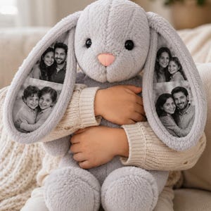 Puede incluir: Un juguete de peluche de conejo gris claro con orejas largas y suaves. Cada oreja muestra dos fotografías en blanco y negro de personas. El conejo tiene ojos oscuros y redondos y una pequeña nariz rosa claro, con un acabado de tela texturizada.