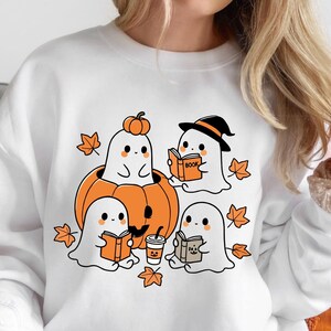 May include: White sweatshirt with a graphic of four ghosts reading books and sitting on a pumpkin. The ghosts are wearing witch hats and holding books that say "Book" and "Boo".