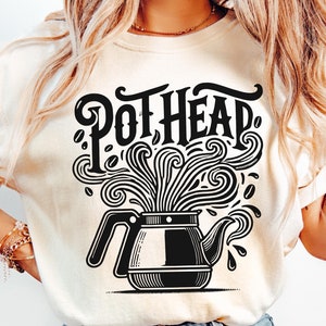 May include: A white t-shirt with a black graphic of a teapot with steam coming out of the spout. The text "Pothead" is written in a stylized font above the teapot.