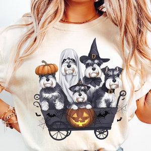 May include: A white t-shirt with a graphic of five miniature schnauzers dressed in Halloween costumes riding in a wagon with a jack-o-lantern.