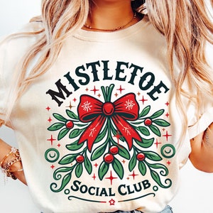 May include: A white t-shirt with a green mistletoe design and the text "Mistletoe Social Club".