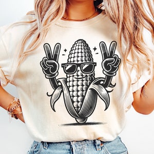 May include: A white t-shirt with a black and white illustration of a corn cob wearing sunglasses and making the peace sign with both hands.