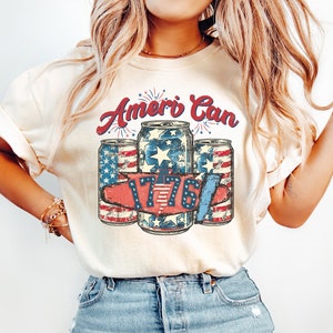 May include: A white t-shirt with a vintage-style graphic of four red, white and blue cans with the text "Ameri Can" and "1776" above them.