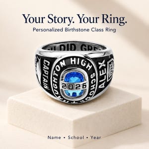Puede incluir: Un anillo de graduación plateado con una piedra azul ovalada central, el texto "NAUGHTON HIGH SCHOOL" y "2026" en la cara, y "CAPTAIN" y "ALEX" grabados en los laterales. La banda interior tiene la inscripción "YOU DID GREAT".