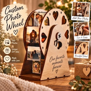 Puede incluir: Un expositor de fotos de madera con forma de noria, con recortes en forma de corazón y ranuras para varias fotografías. La base tiene grabado el texto "Our favorite moments forever" y un símbolo de corazón.
