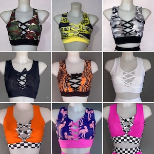 Op de afbeelding: Negen verschillende crop tops met een kruislings veterontwerp aan de voorkant. De tops zijn in verschillende kleuren en patronen, waaronder camouflage, geel en zwart waarschuwingslint, wit, zwart, oranje en zwarte slangenprint, roze en blauwe flamingo print, en roze met zwart-witte ruit.