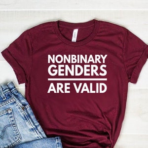 May include: A maroon t-shirt with the text "Nonbinary Genders Are Valid" in white lettering.