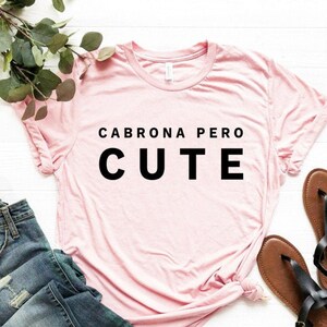 May include: A pink t-shirt with the text "CABRONA PERO CUTE" printed in black.
