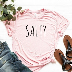 May include: A pink t-shirt with the word "SALTY" printed in black on the front.