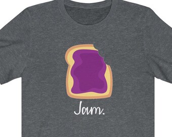 May include: A dark heather gray short-sleeve t-shirt featuring a graphic of a slice of toast with purple jam and a bite taken out of the top right corner. Below the toast, the word Jam is printed in a white, handwritten-style script font.