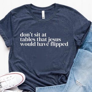 May include: A navy blue t-shirt with the text "don't sit at tables that jesus would have flipped" in white lettering.
