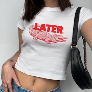 May include: White cropped t-shirt with a red alligator graphic and the word "LATER" printed in red.