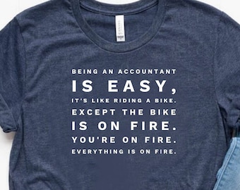 May include: A navy blue t-shirt with white text that reads "Being an accountant is easy, it's like riding a bike. Except the bike is on fire. You're on fire. Everything is on fire."